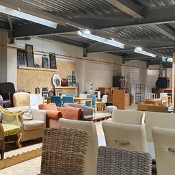 Winkelvloer met diverse meubels: stoelen, tafels, kasten en andere huisraad uitgestald in een groot pand