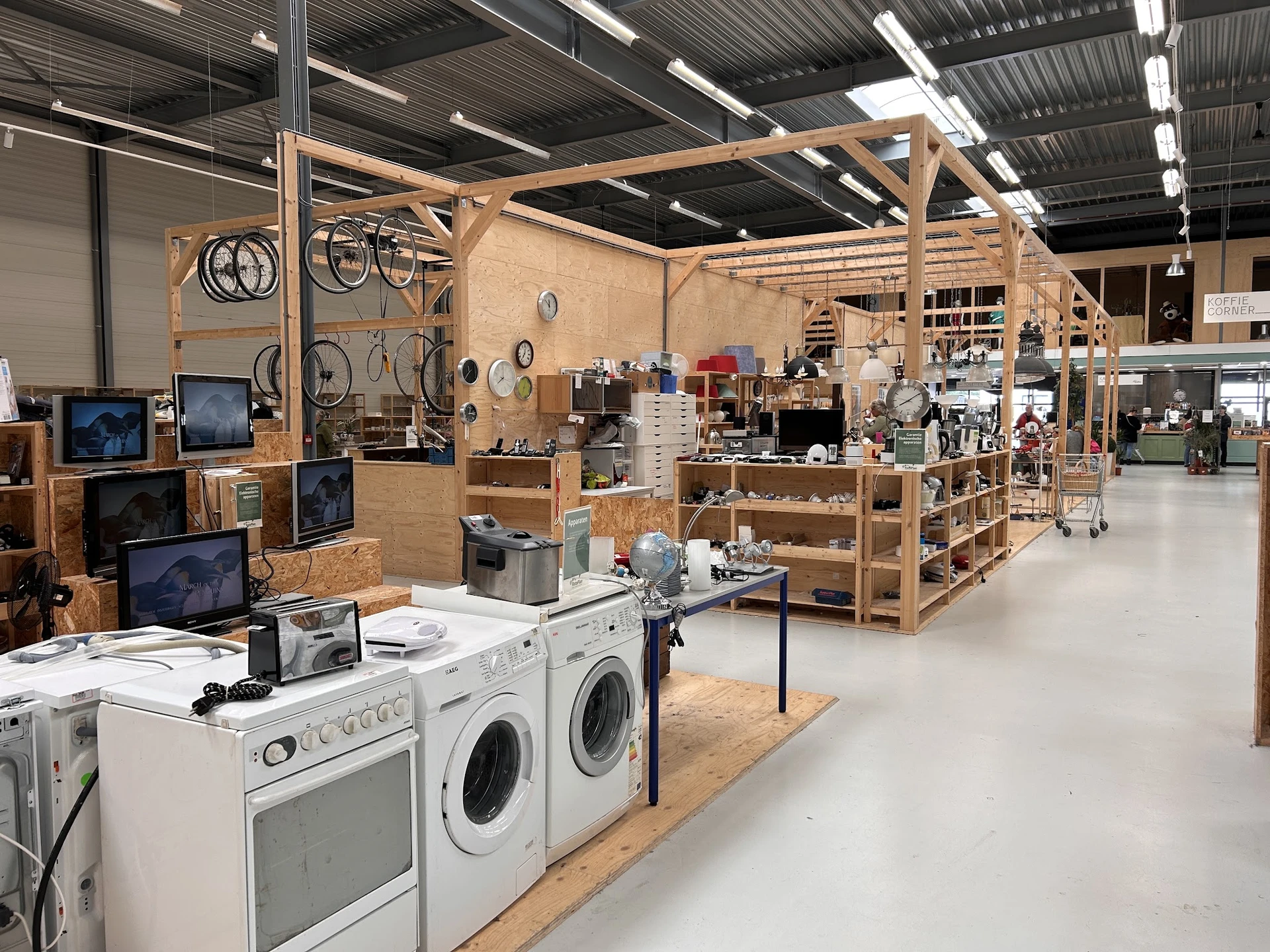 Ruime winkelhal met houten stellingen vol huishoudelijke artikelen, elektronica en gebruikte goederen