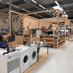 Ruime winkelhal met houten stellingen vol huishoudelijke artikelen, elektronica en gebruikte goederen