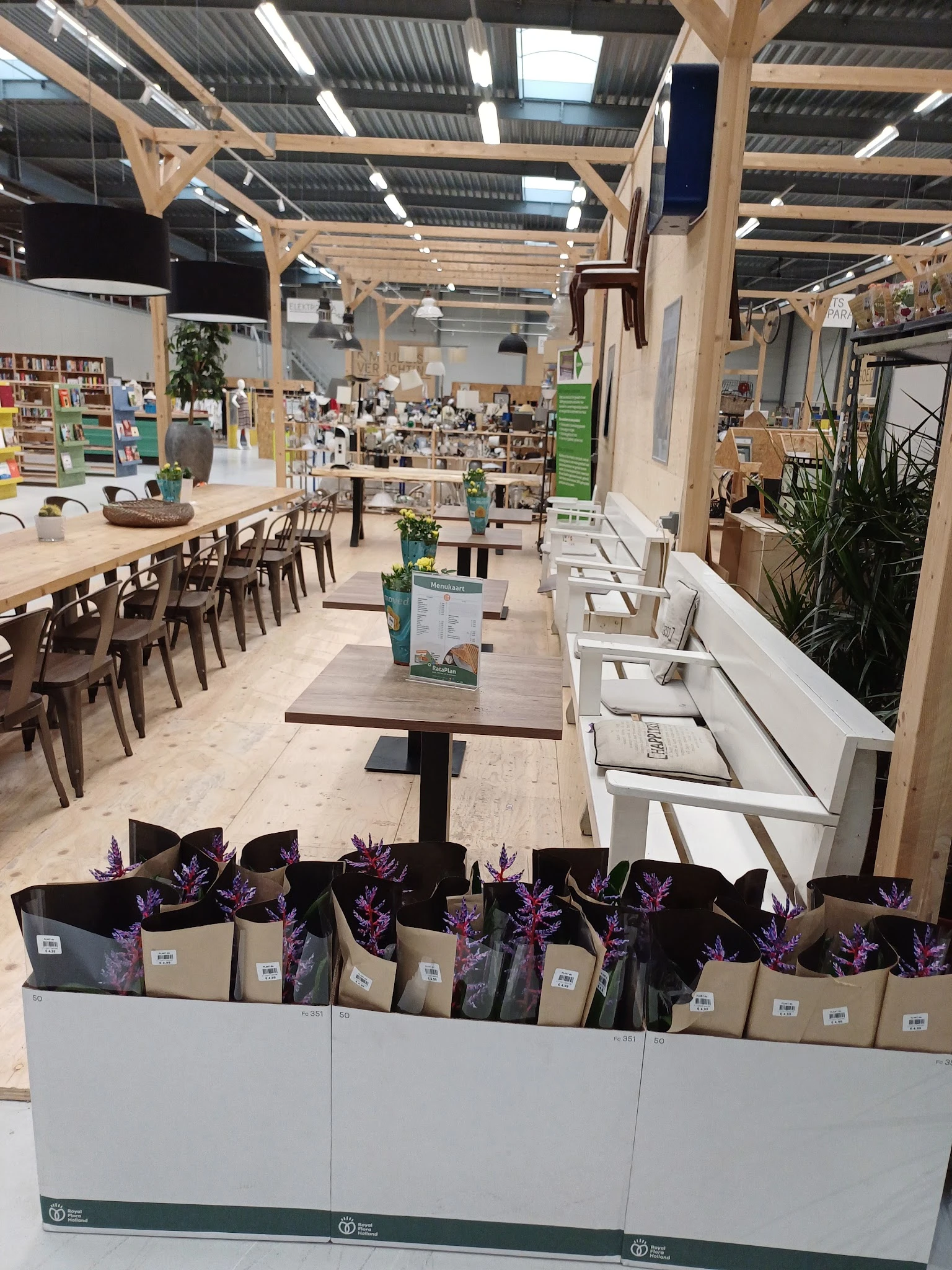 Winkelinterieur met tafels, stoelen, bloemen in dozen en stellingen met spullen op de achtergrond