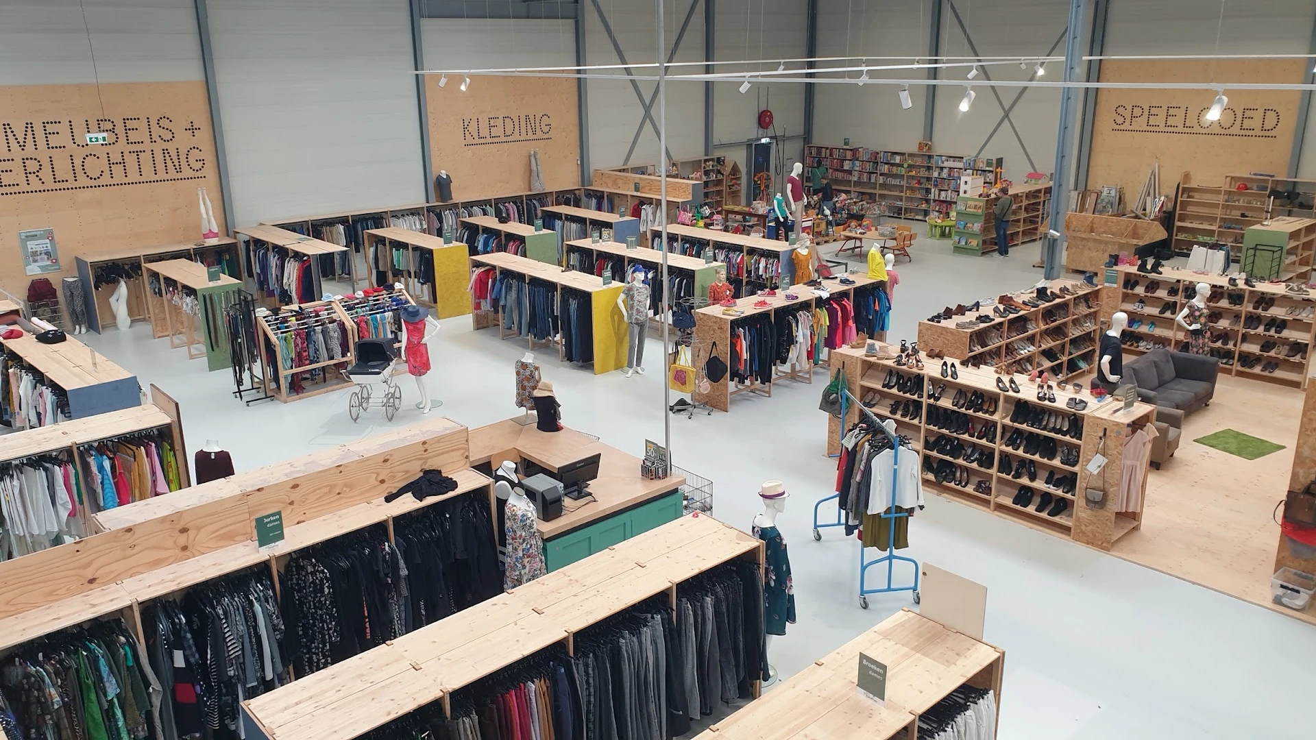 Overzicht van kringloopwinkel met kledingrekken, boekenkast en winkelafdelingen