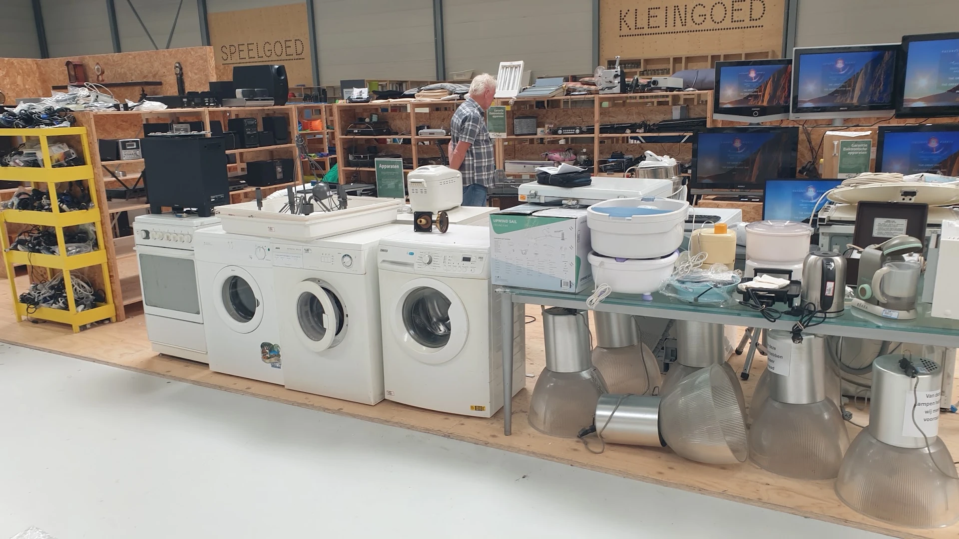 Uitgestalde witgoed en huishoudelijke apparaten in een kringloopwinkel, waaronder wasmachines, drogers en andere electronica