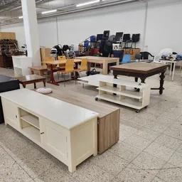 Meubels in een kringloopwinkel: kasten, tafels, stoelen en een biljart uitgestald op de vloer