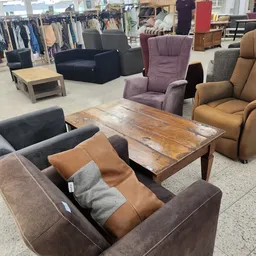 Inrichting van kringloopwinkel met diverse meubels: bruine en grijze stoelen, paarse fauteuil, houten tafel en stellingen met