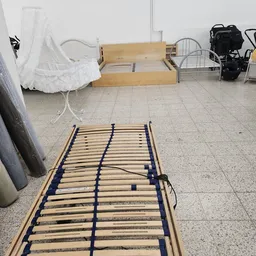Houten lattenbodem voor bed met blauwe elastische banden, op betonnen vloer