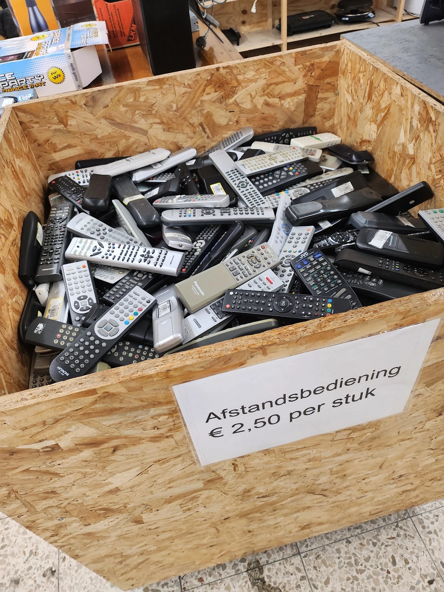 Houten bak met grote hoeveelheid afstandsbedieningen, prijskaartje toont €2,50 per stuk