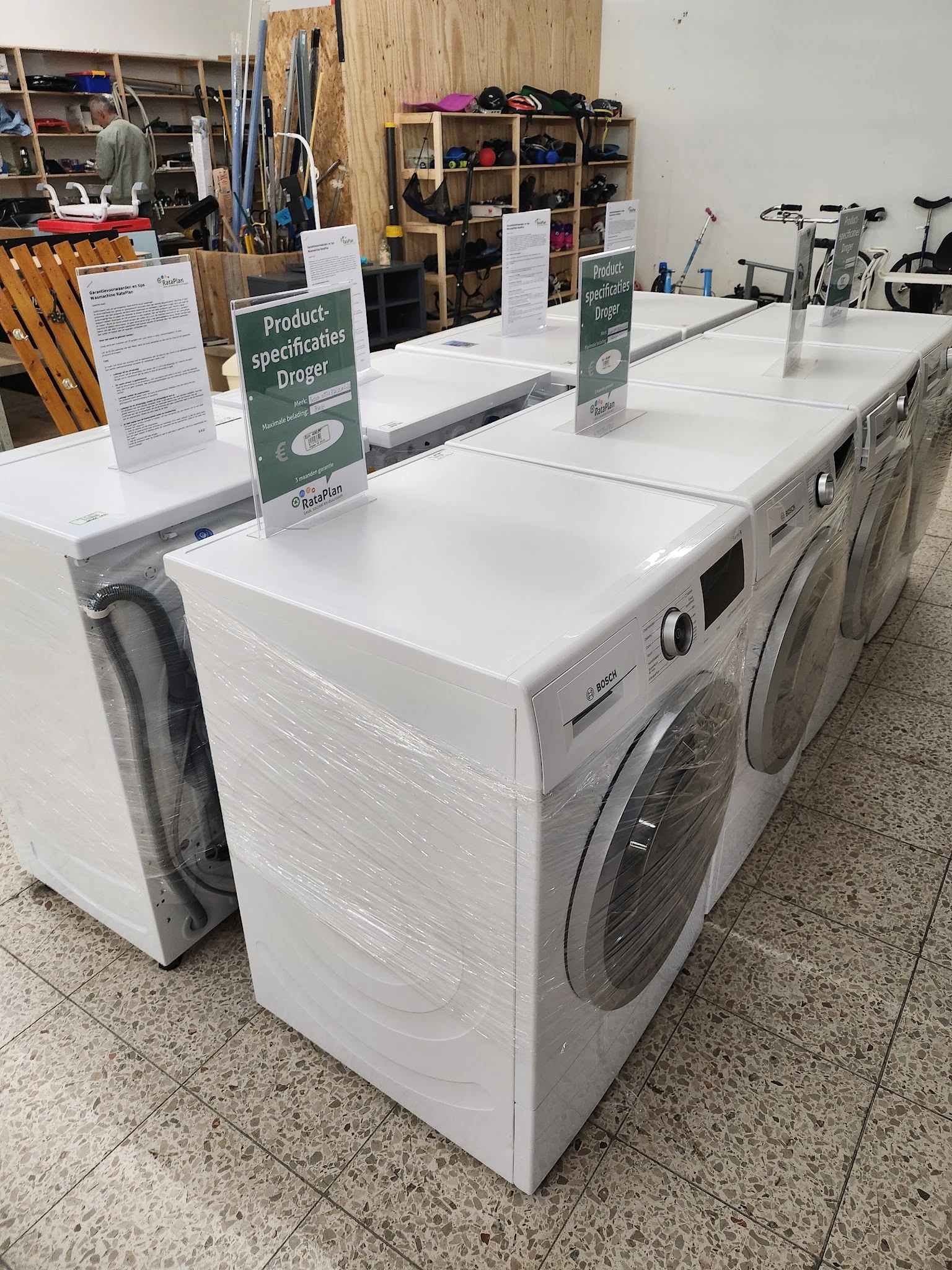 Rij met witte wasmachines en droogkasten in de winkel met informatiebordje