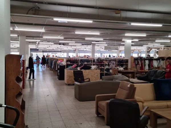Ruime winkelvloer met meubels, rekken met kleding en diverse spullen onder heldere verlichting