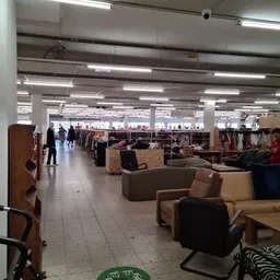 Ruime winkelvloer met meubels, rekken met kleding en diverse spullen onder heldere verlichting