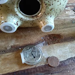 Close-up van een keramiek object met ogen, munten en andere items op hout