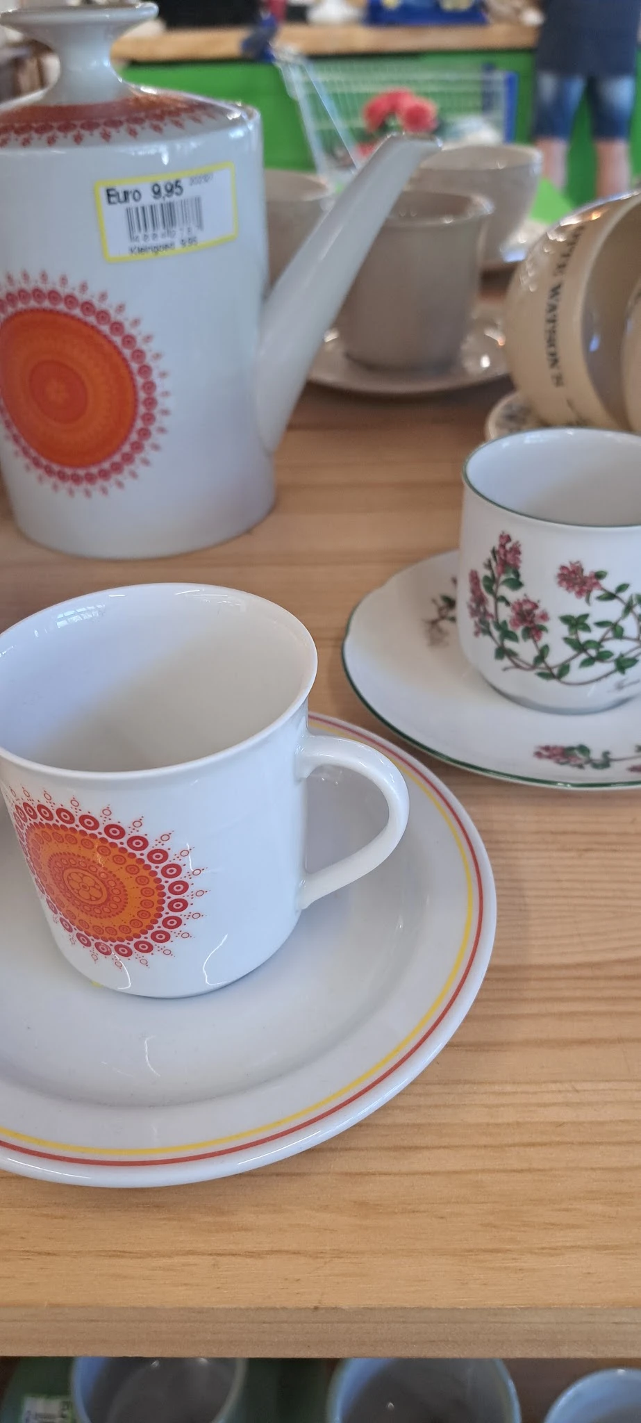 Close-up van servies: witte mok met oranje mandalapatroon en bord met roze bloemenranken