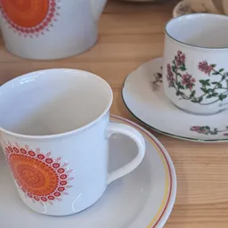 Close-up van servies: witte mok met oranje mandalapatroon en bord met roze bloemenranken
