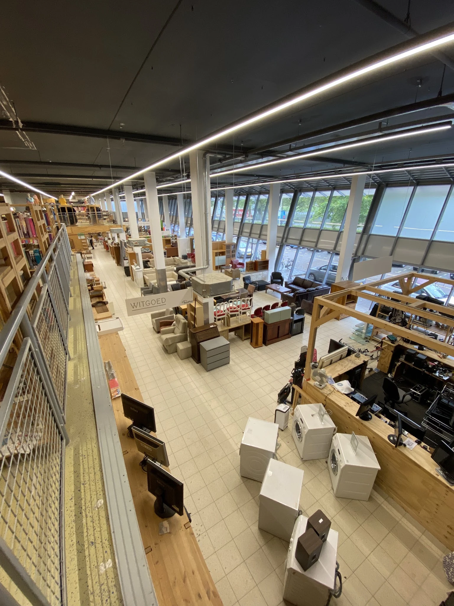 Ruim en helder winkelinterieur met stellingen, meubels en diverse tweedehandsartikelen verspreid over de vloer