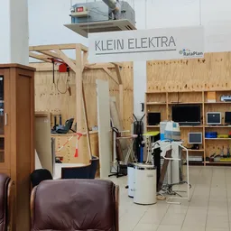 Werkruimte in kringloopwinkel met houten stellingen, gereedschapsbord, elektronicaonderdelen en bruine fauteuils op de voorgr