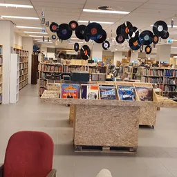 Winkelvloer met boekenrekken, vinyl-platen als decoratie aan het plafond en een rode stoel op de voorgrond