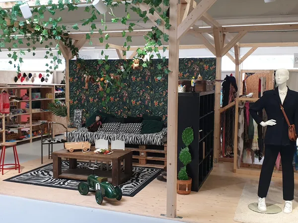 Winkelinterieur met decoratief bed, kledingrekken, mannequin met zwart pak, en groen bladerdecor
