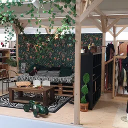 Winkelinterieur met decoratief bed, kledingrekken, mannequin met zwart pak, en groen bladerdecor