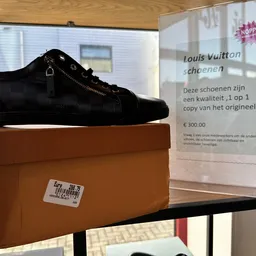 Zwarte suède schoenen op bruine doos met informatiebord en prijskaart