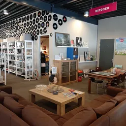 Winkelvloer met bruine zithoeken, houten tafel, witte stellingen met huishoudartikelen en decoratieve borden aan het plafond