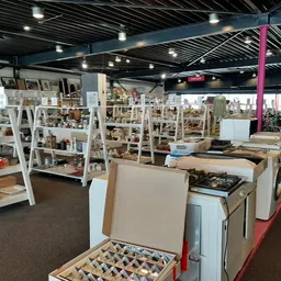 Winkelvloer van kringloopwinkel met witte stellingen vol gebruiksspullen, huishoudartikelen en diverse koopwaar