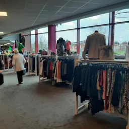 Winkelvloer met kledingrekken vol tweedehands kleding, grote ramen en winkelmeubels