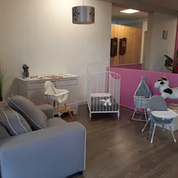 Winkelvloer met grijze bank, speelhoek met wit babybedje, roze afscheiding en kinderspeelgoed