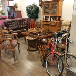 Ingerichte woonkamer met bruine leren bank, houten stoelen, salontafel en een rode fiets in een kringloopwinkel