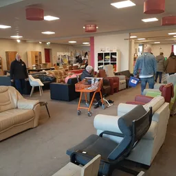Ruim winkelinterieur met diverse meubels zoals banken, fauteuils en stoelen, bezoekers wandelen rond tussen de stellingen