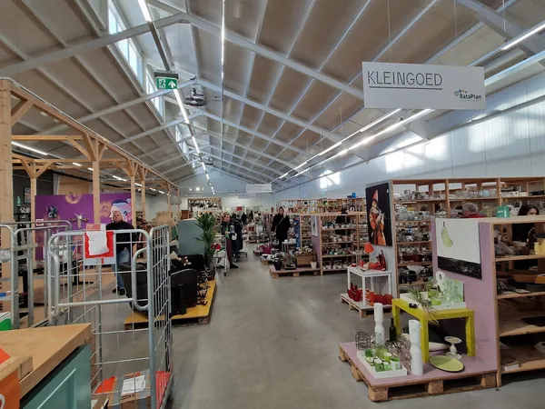 Overzicht van de winkelvloer met stellingen, uitgestalde spullen en bezoekers in een kringloopwinkel