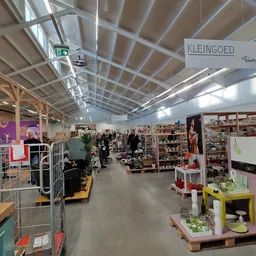 Ruim winkelbinnenland van kringloopwinkel met stellingen, display-boxen en diverse artikelen langs het gangpad