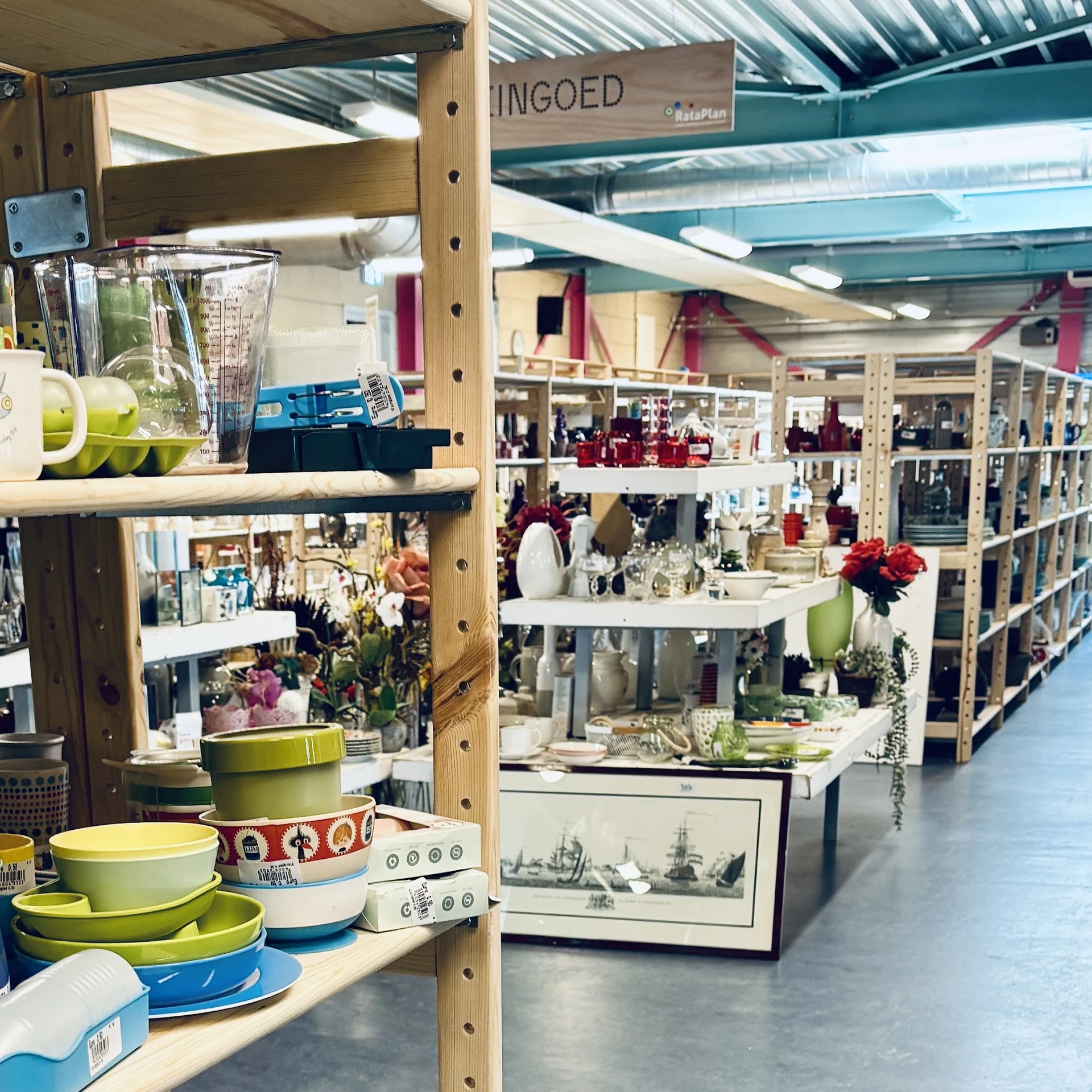 Winkelvloer met houten stellingen vol huishoudelijke artikelen, servies, decoratie en diverse spullen.
