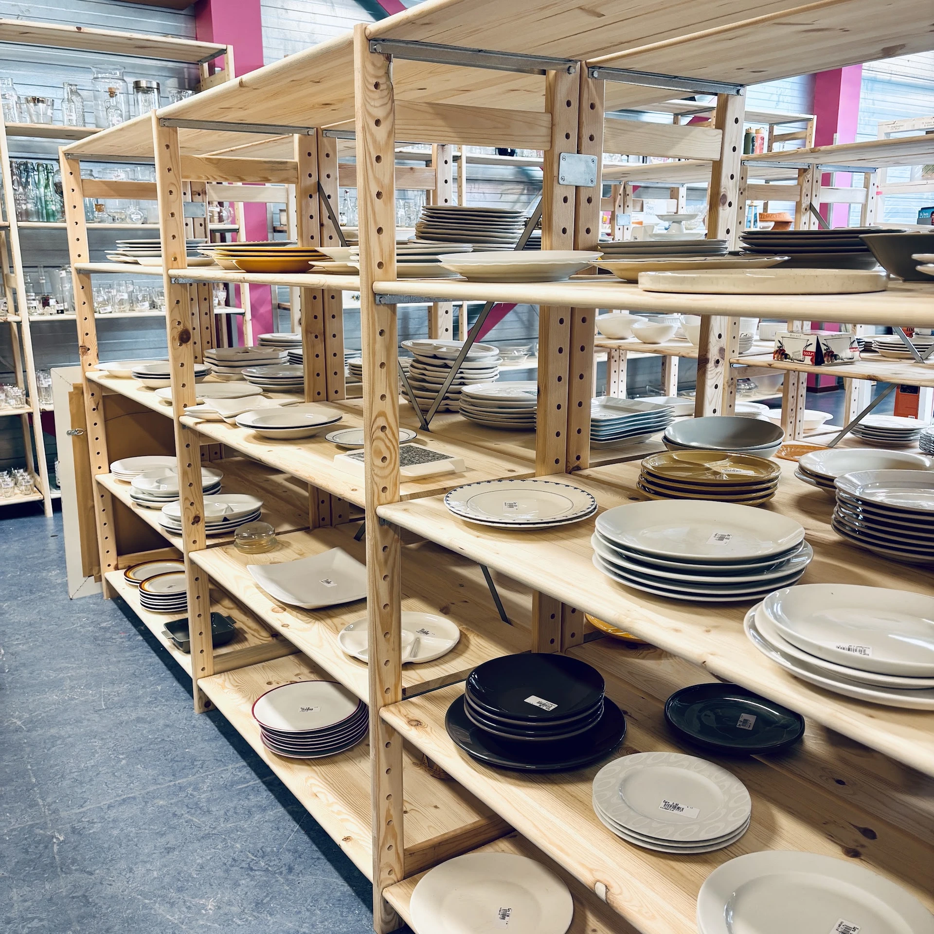 Houten stellingen gevuld met diverse serviesgoed, borden en schalen in verschillende kleuren en maten