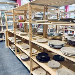 Houten stellingen gevuld met diverse serviesgoed, borden en schalen in verschillende kleuren en maten