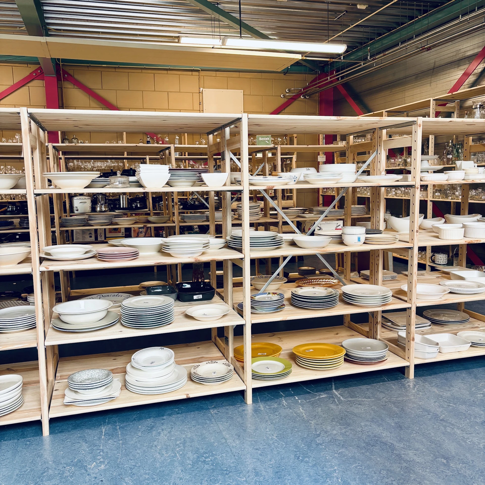 Houten stellingen met uitgestalde serviesgoed: stapels borden, schalen en ander tafelservies in wit, blauw en geel