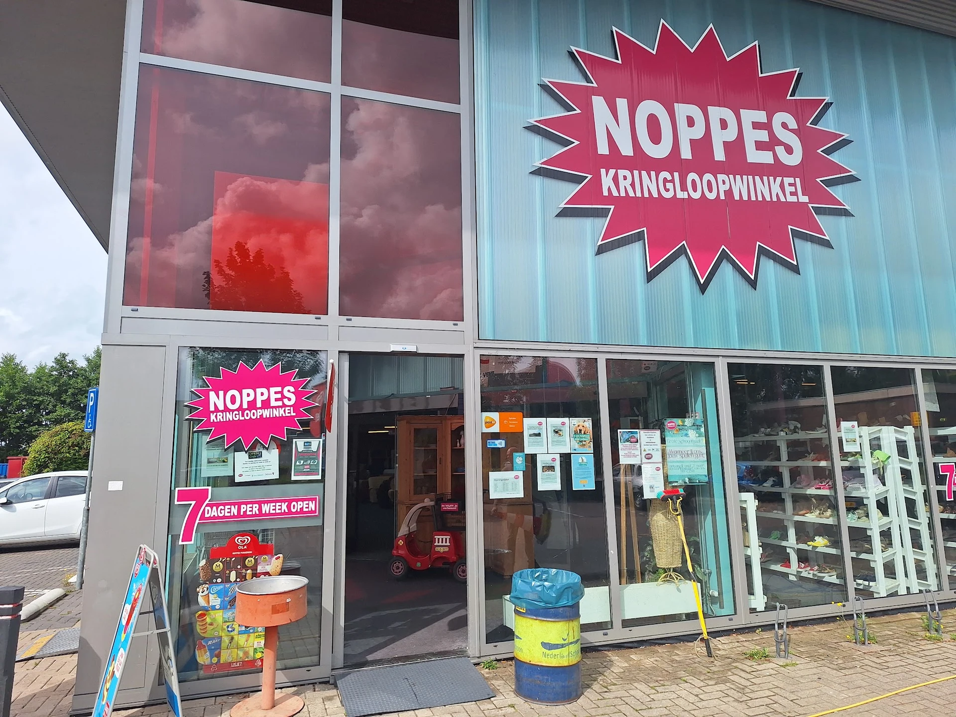Gevel van kringloopwinkel Noppes met roze uithangteken, ingang en etalageruiten