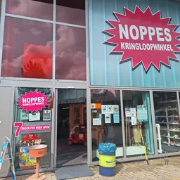 Gevel van kringloopwinkel Noppes met roze uithangteken, ingang en etalageruiten