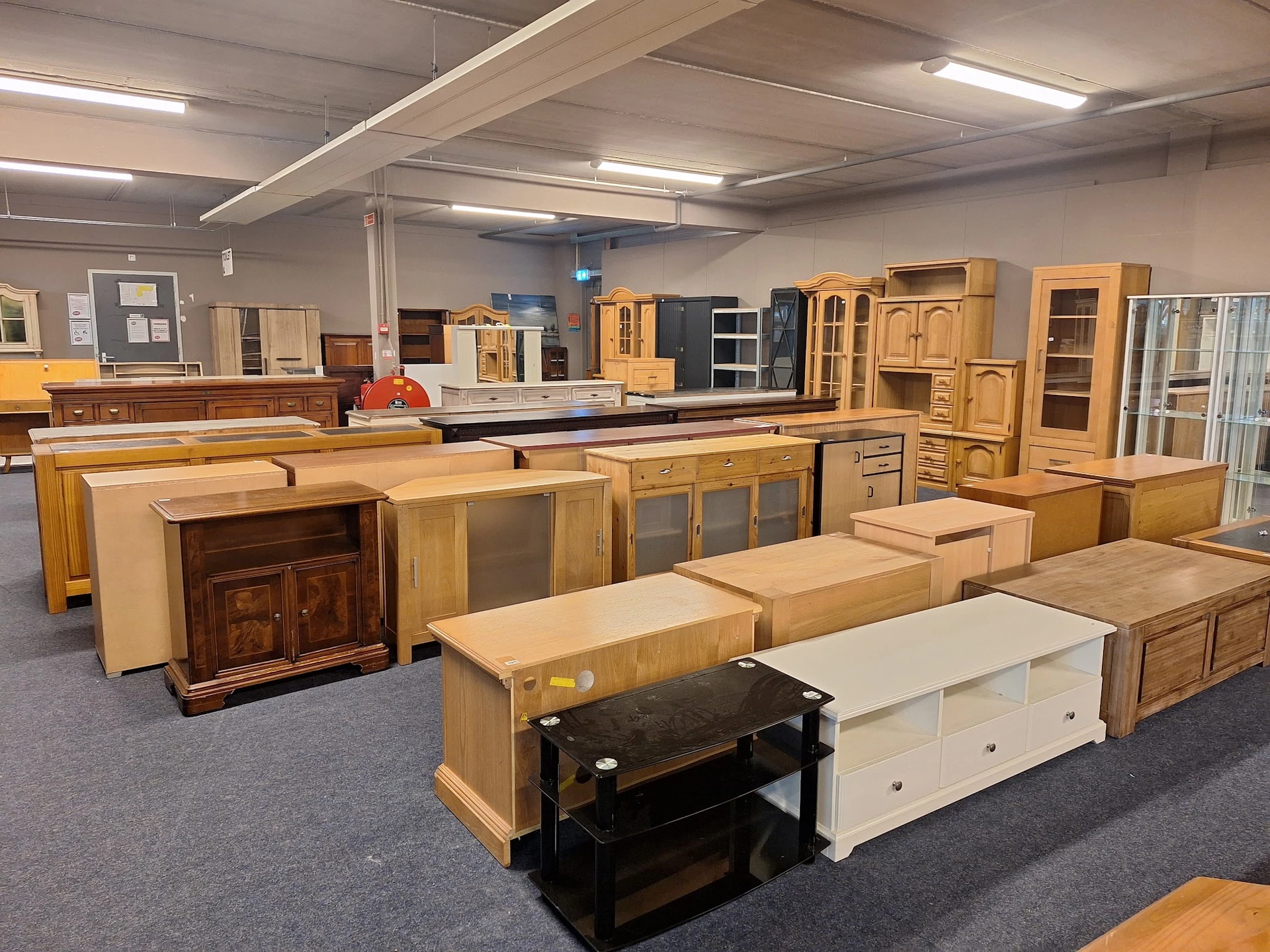 Showroom met diverse houten kasten, kastjes en meubelstukken uitgestald op grijze vloer