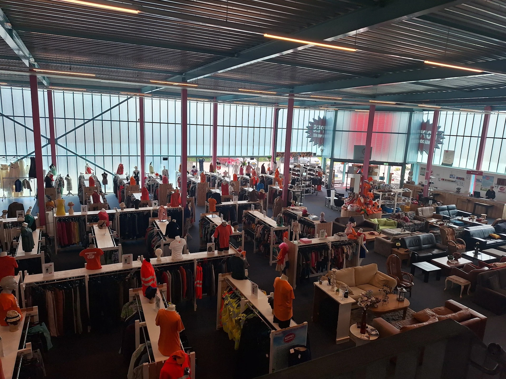 Ruim winkelinterieur met kledingrekken, mannequins en winkelassortiment onder glazen dak