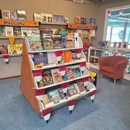 Winkelinterieur met boekenrek op wielen en wandkasten vol boeken en posters, oranje stoeltje op de achtergrond