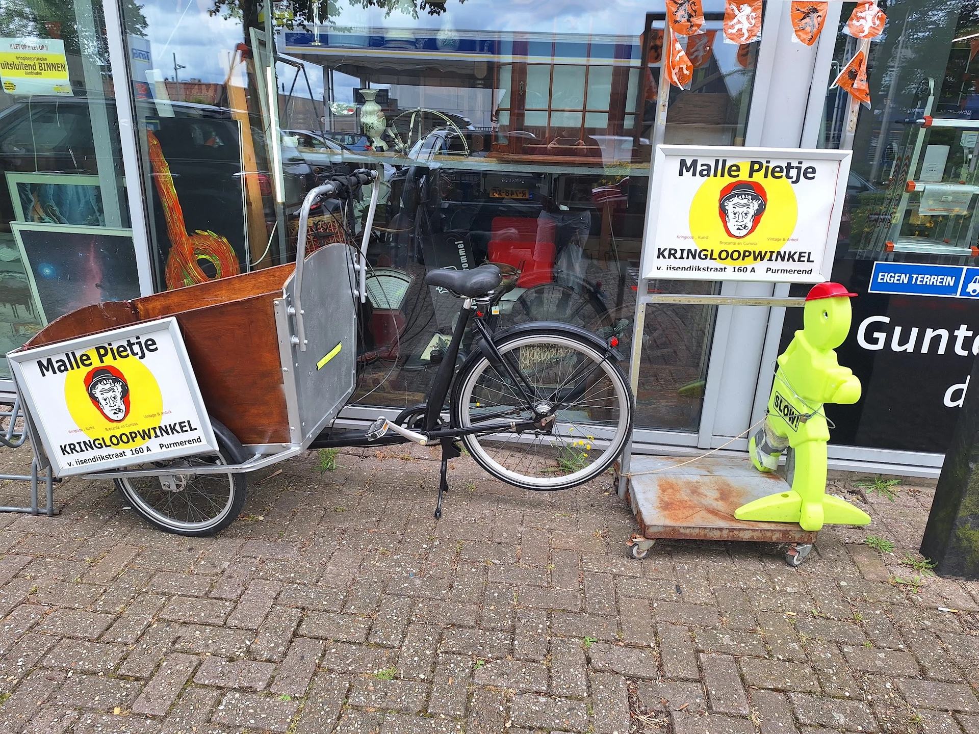 Winkelpui met etalage waarin fietsen en tweedehands spullen; logo's van Malle Pietje zichtbaar op ramen