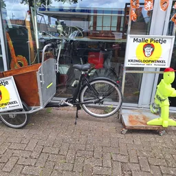 Winkelpui met etalage waarin fietsen en tweedehands spullen; logo's van Malle Pietje zichtbaar op ramen
