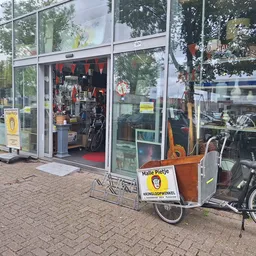 Voorkant van kringloopwinkel met grote glazen pui, fietsen ernaast geparkeerd en een geel bord met Malle Pietje logo