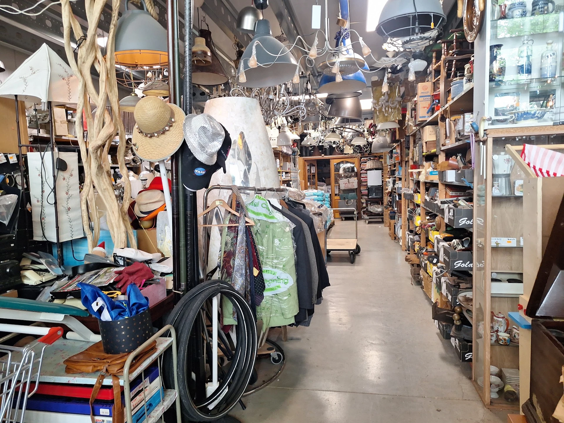 Winkelvloer van kringloopwinkel met stellingen vol spullen, hangende lampen en kleding