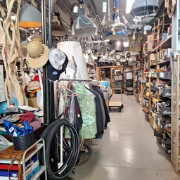 Winkelvloer van kringloopwinkel met stellingen vol spullen, hangende lampen en kleding