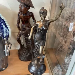 Bronzen beeldhouwwerk van een vrouw met opgeheven arm naast een ander bronsbeeldhouwwerk