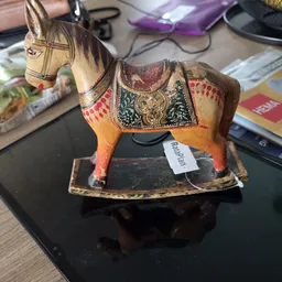 Houten decoratief paard met beschilderde zadel en decoraties, op een zwarte onderbasis