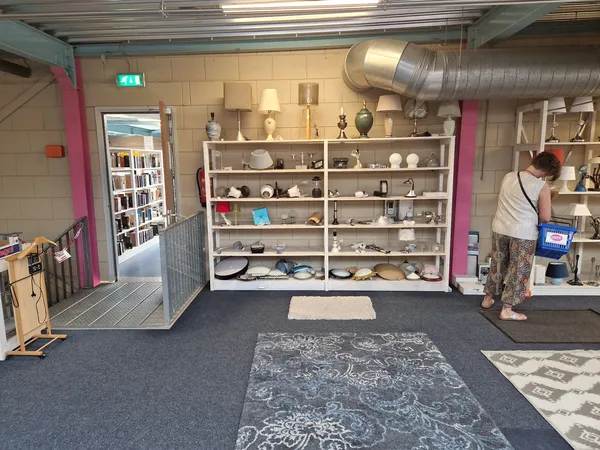 Winkelvloer met stellingen vol serviesgoed, boeken en huishoudartikelen, een persoon aan het werk rechts