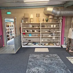 Winkelvloer met stellingen vol serviesgoed, boeken en huishoudartikelen, een persoon aan het werk rechts