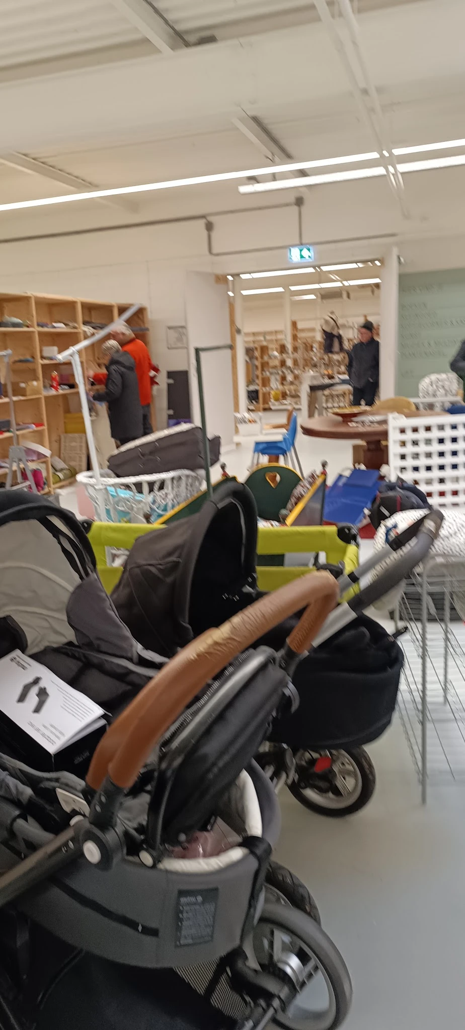 Winkelvloer met kinderwagens, dozen en diverse spullen, mensen op achtergrond