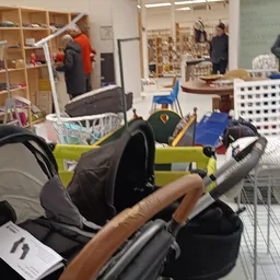 Winkelvloer met kinderwagens, dozen en diverse spullen, mensen op achtergrond